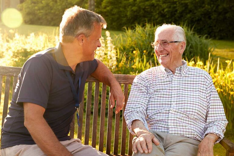 Older adults talking together in a bright common room while one resident joins a small group activity.